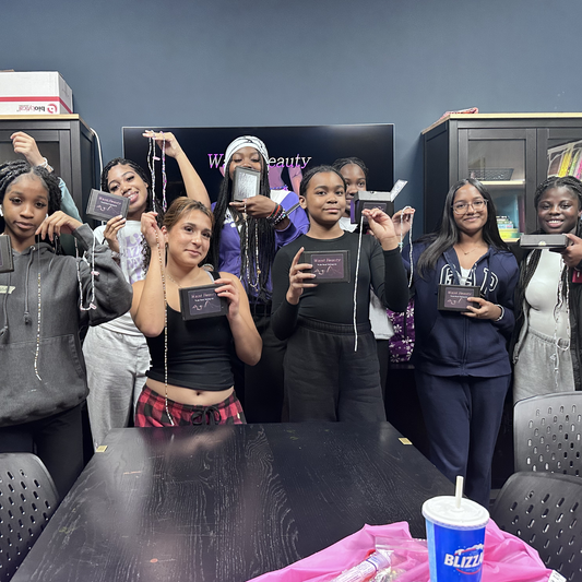 Group of people holding finished waist bead products in a room with a TV screen displaying 'Waist Beauty' post workshop