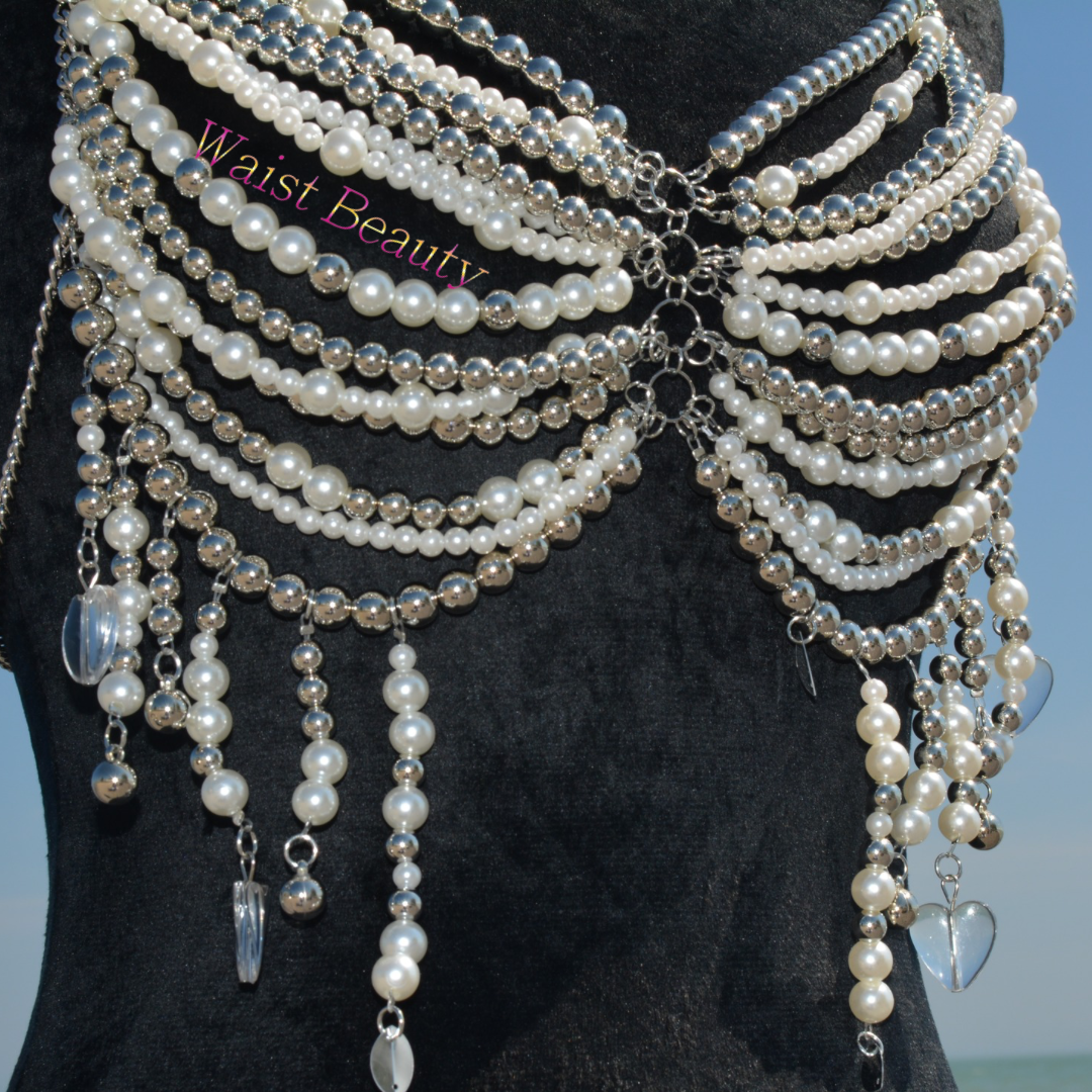 Waist Beauty Beaded Top - Metallic silver and pearl layered body chain bra with dangling heart charms displayed on a black mannequin at a rocky beach.