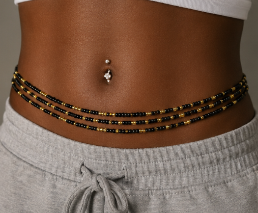 A close-up of a person's lower torso wearing a multi-strand beaded waist chain with black and gold beads, paired with gray sweatpants and a white top. by waist beauty