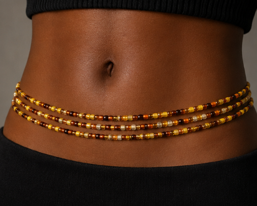 A close-up of a model's waist wearing a multi-strand beaded waist chain with amber, gold, and brown beads.