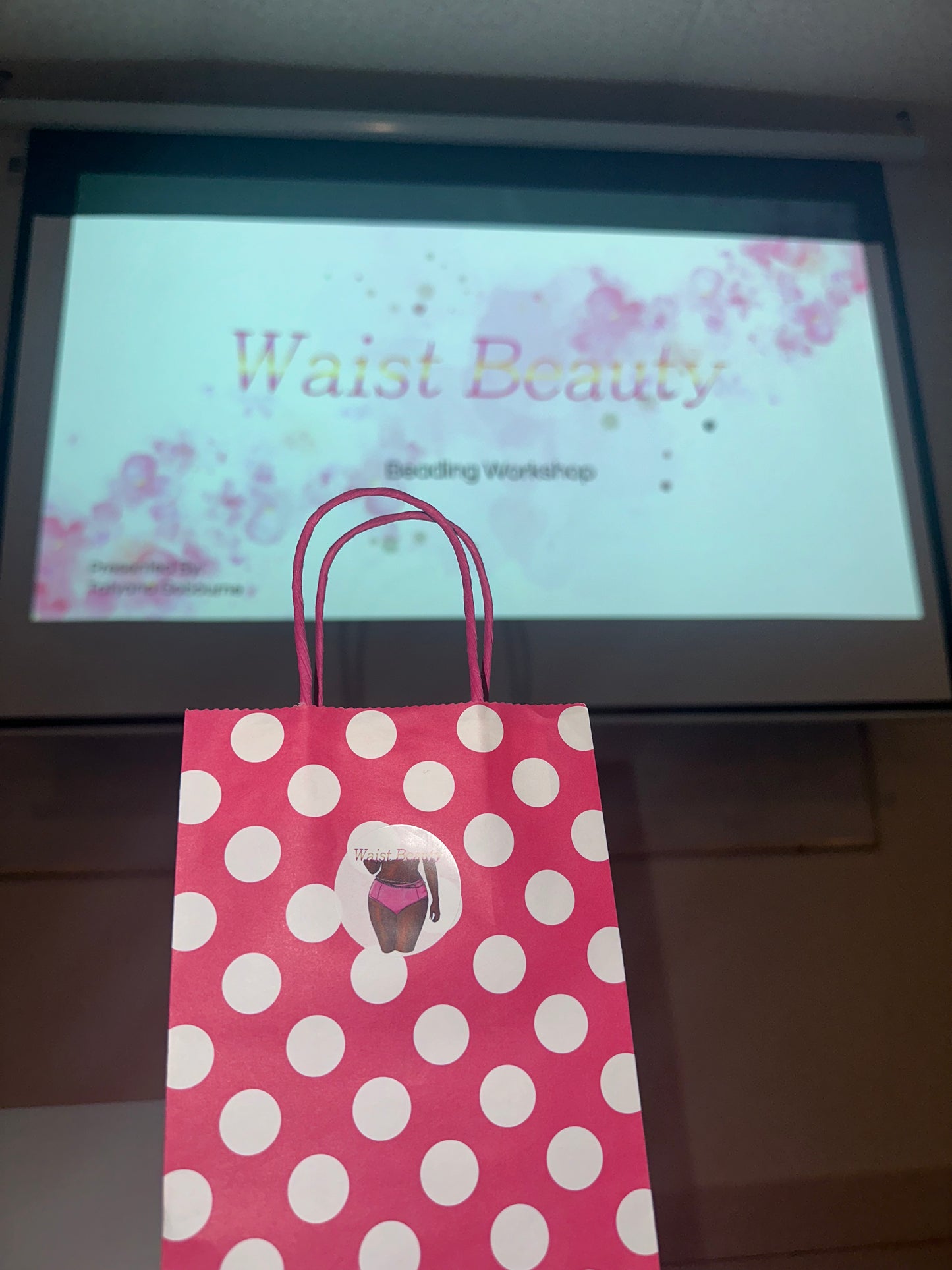 Pink polka dot gift bag with a projection screen displaying 'Waist Beauty' in the background
