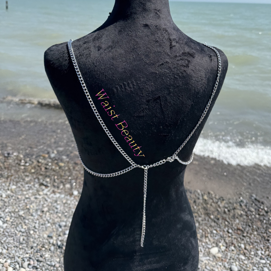 Waist Beauty’s new beaded bra - Metallic silver and pearl layered body chain bra with dangling heart charms displayed on a black mannequin at a rocky beach.