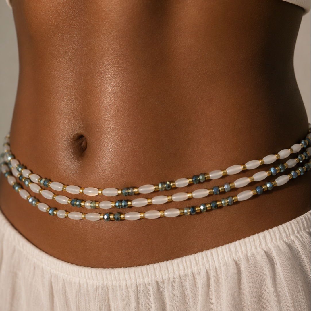 A close-up of a model's waist wearing a multi-strand beaded waist chain. The chain features translucent white beads, small metallic gold spacer beads, and blue-green faceted beads. by waist beauty