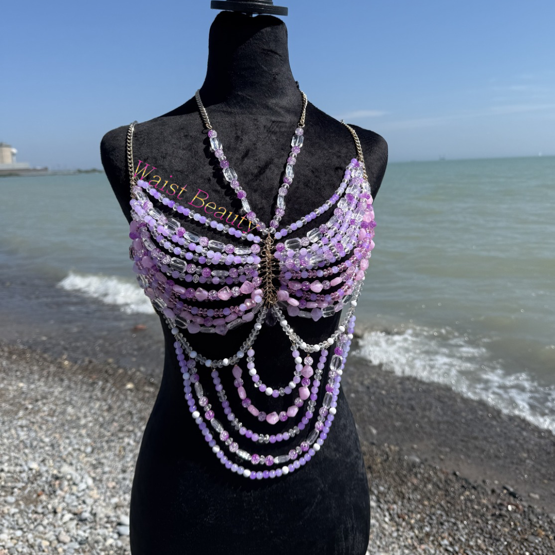 Intricate purple and lavender crystal beaded body chain top with a cascading midriff drape on a black mannequin by the sea.