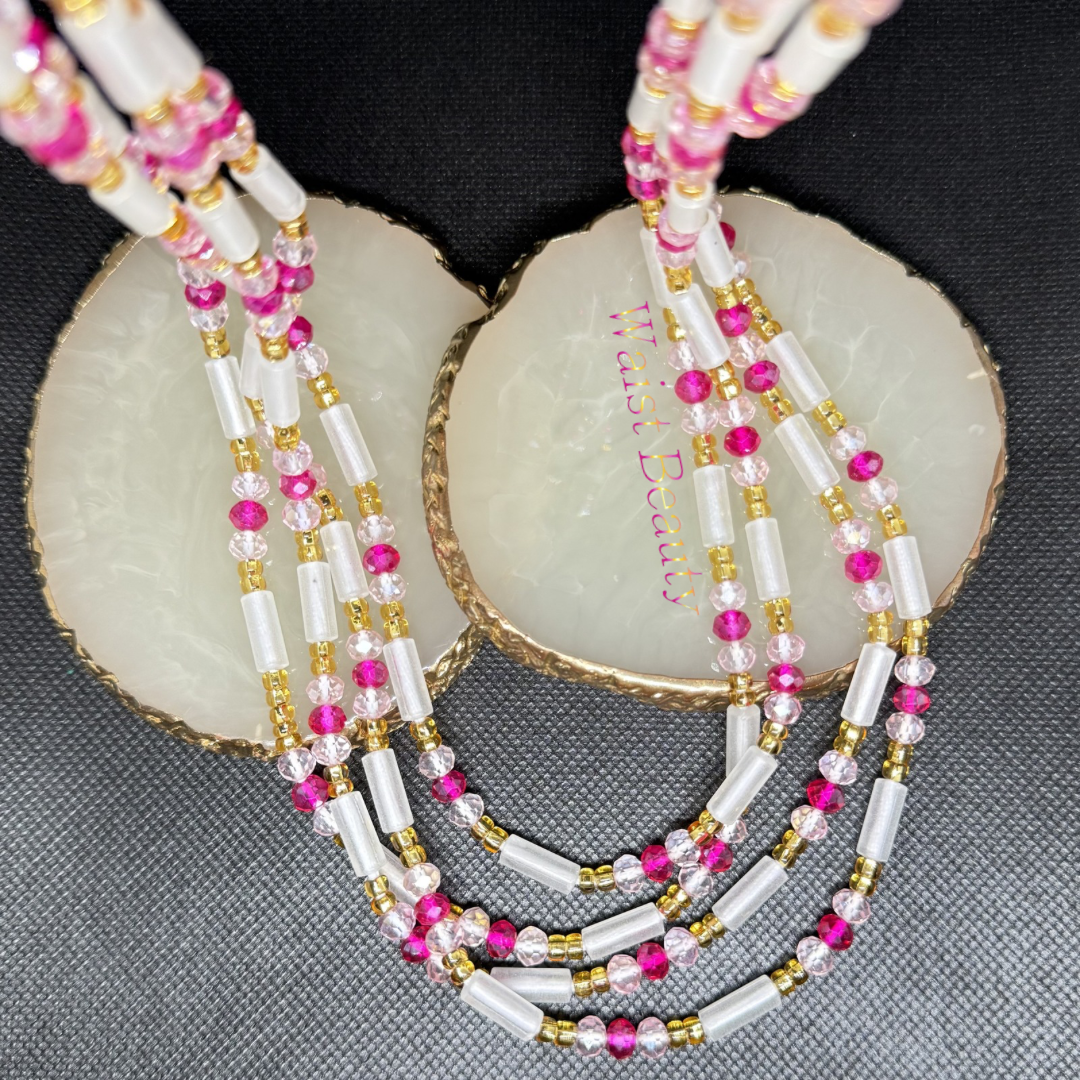 Flirty, vibrant, and fun, the Fuchsia Fizz tie-on waist beads add a perfect pop of color to your everyday look. This design features frosty white cylinder glass beads beautifully balanced by clear-pink rondelles and eye-catching hot fuchsia crystals. Wrapped in a delicate frame of gold seed beads, this 53-inch piece represents femininity, care, and romance—making it a perfect gift for yourself or someone special.