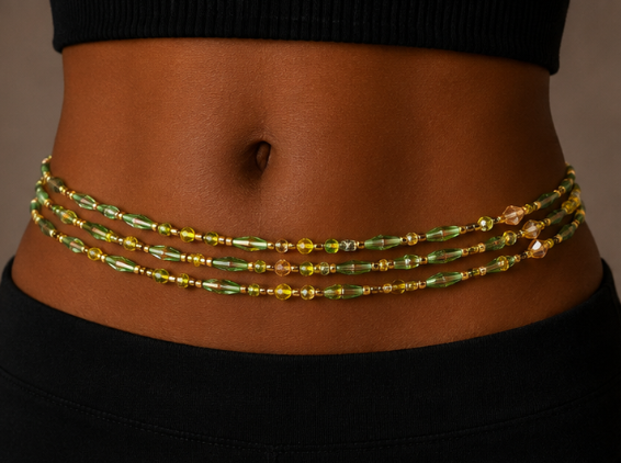 A close-up of a model's midsection wearing a three-strand beaded waist chain with green and gold beads.
