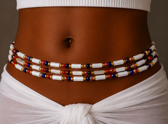 A close-up of a model's midsection wearing a multi-strand beaded waist chain. The waist chain features alternating white cylindrical beads and small red, blue, and gold metallic beads.