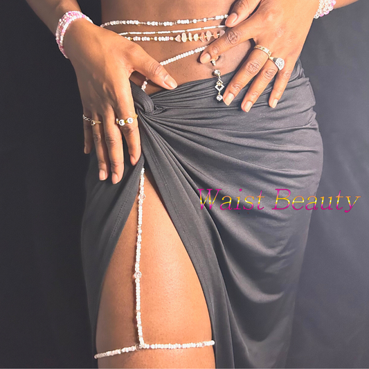 A close-up image of a thigh/waist bead decorated with pink and white beads, worn by a person against a dark background.